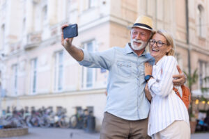A joyous elderly couple taking a selfie, capturing precious moments while enjoying urban exploration in front of a building and row of parked bicycles, showing care and happiness.