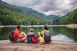 Family with a small yellow dog resting on a pier and looking at lake and foggy mountains
